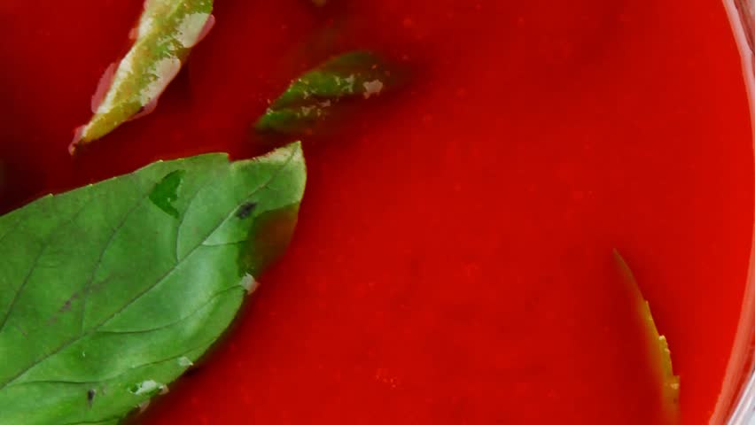 cold fresh diet tomato soup with basil thyme and raw tomatoes in transparent bowl over red mat on wood table ready to eat 1920x1080 intro motion slow hidef hd