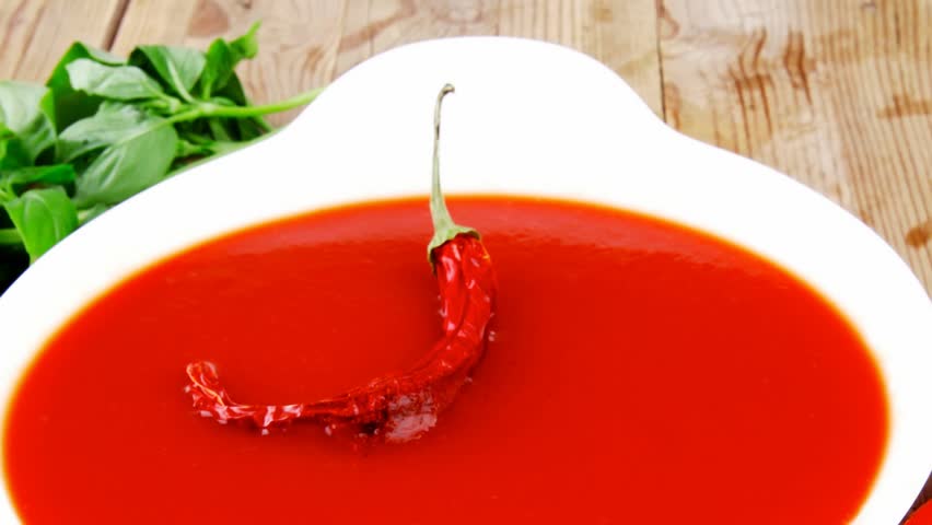 diet food : hot tomato vegetable soup with basil thyme and raw tomatoes in white round bowl over red mat on wood table ready to eat 1920x1080 intro motion slow hidef hd