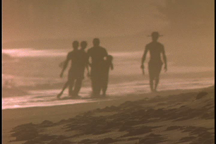 Slavery reenactment in Ghana, Africa. MS silhouette of overseer leading five men in chains (two are boys) up beach in very bright sunlight. 