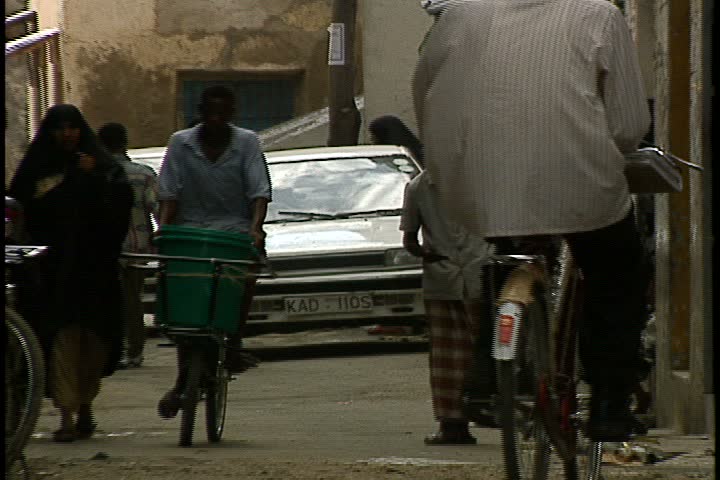 MOMBASA, KENYA, AFRICA - DECEMBER 01, 1998: Street scenes in Mombasa; LS women dressed head to toe in black niqab walk through busy alley way with children. 