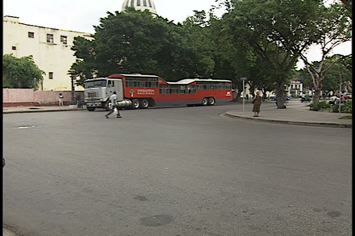 HAVANA, CUBA - SEPTEMBER 15, 2000: Street scenes in La Habana Vieja; WS big red camel bus approaches and passes camera, then stops for passengers waiting at bus stop.