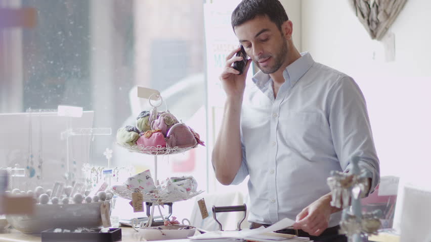 An attractive male store owner makes a phone call at work, possibly to his suppliers or a business associate. In slow motion.