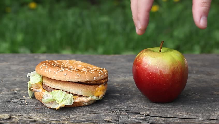 Man's hand choosing burger over apple, unhealthy food 