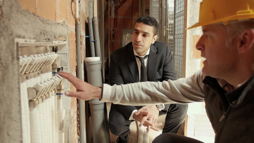 Manual workers, plumber showing drain system pipes to engineer in construction site, new house and building