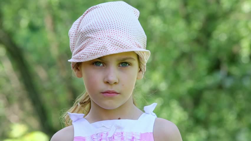 Little girl looks and smiles with panama on head at background of foliage