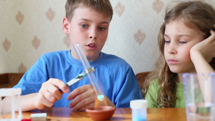 Young boy holds chemical tube above fire and his little sister watches