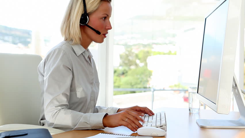 Businesswoman talking on headset and typing at her desk in office
