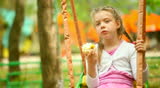 Little girl eating an apple on a swing 