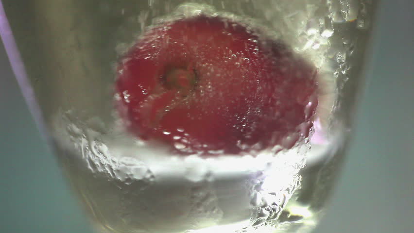 Red grapes falling into glass of golden bubbling champagne