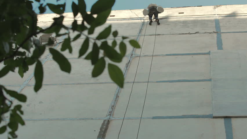 The working man repairs the wall of the house. it is suspended on the ropes