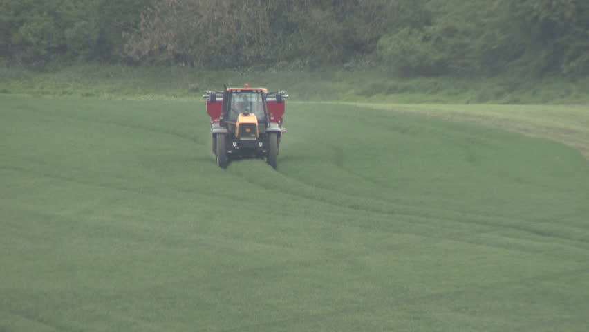 Tractor spraying fertiliser pellets sends up a game bird. HD.