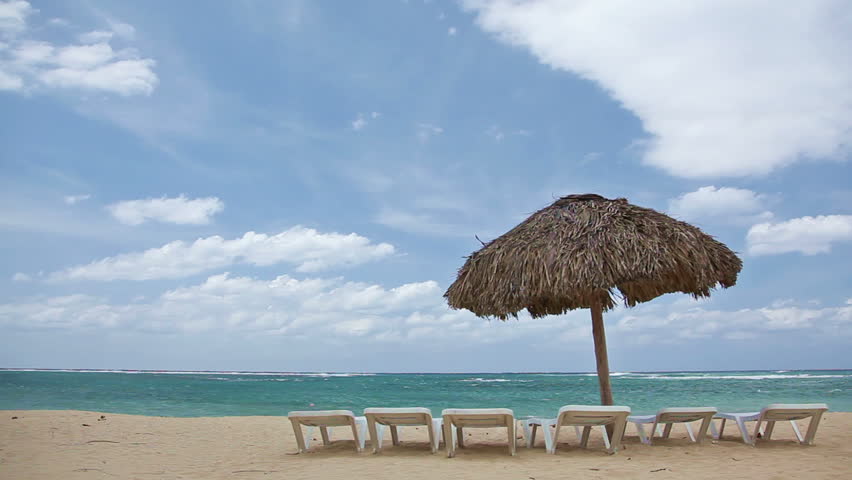 Tropical beach with straw umbrella and chairs around