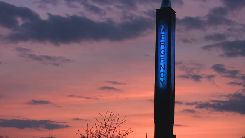 A lit, blue emergency station sign at the University of Guelph, with a sunset sky in the background.