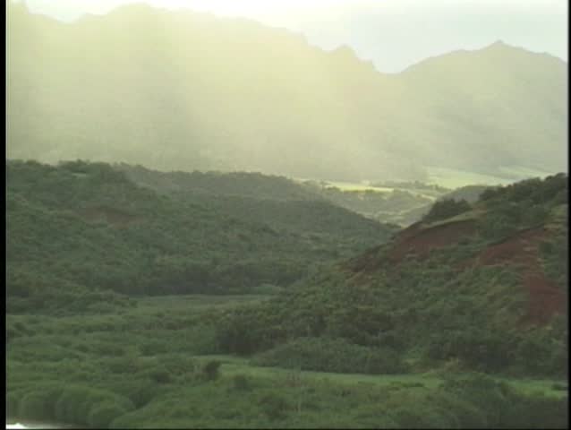 Ancient Hawaiian fish pond at sunset with lush mountain range in the distance.