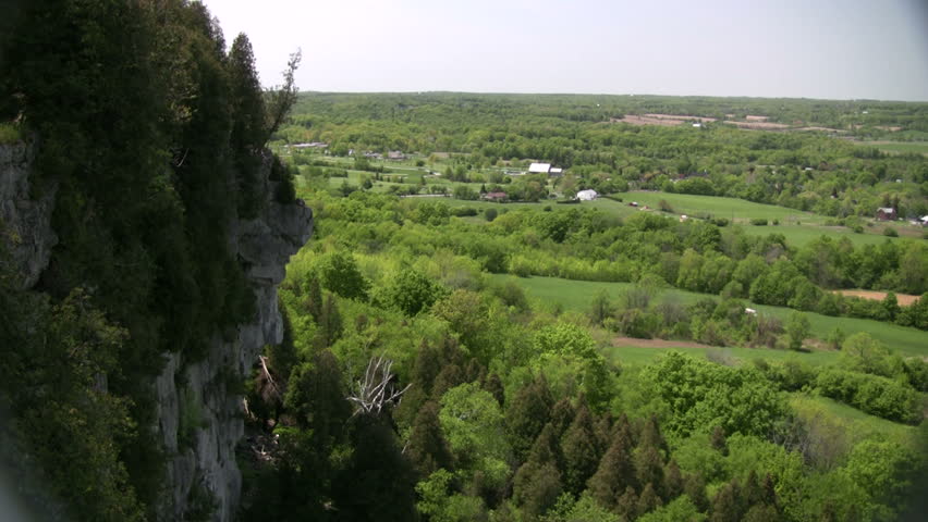 A rocky cliff overlooks the grassy fields and treetops (High Definition)