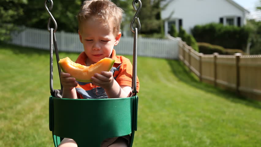 Young boy on swing eating melon