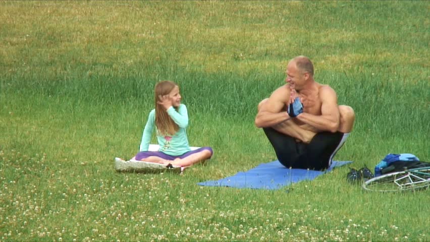Mature man makes yoga in the park. Girl imitates him.