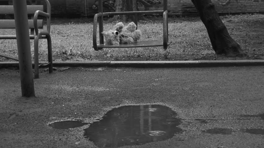 Forgotten Teddy bear on a swing under rain. Deep depression theme. Black and white.