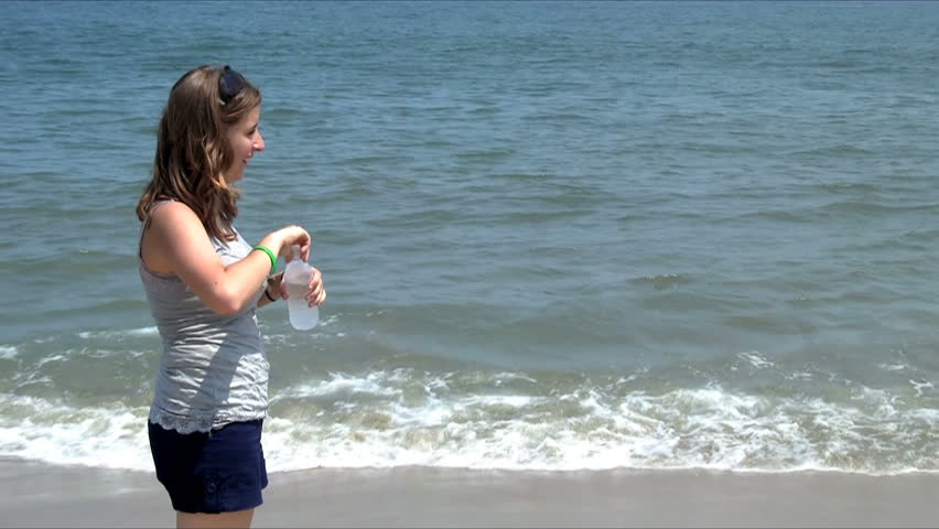 Woman drinking water from a bottle on the beach from the left