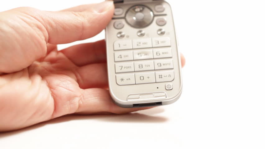 A hand holding a cellular phone, with the other hand making a call, which activates the key back lighting, isolated on white.