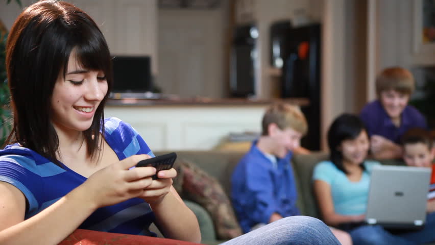 Camera moves from a teenage girl chatting on a cell phone to a group of students on the couch with a laptop. (Rack Focus)