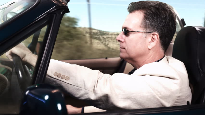 A man driving a sports car while using his cell phone to send a text message.