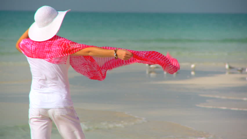 Elegant young female walking on a beautiful white sandy beach looking at aquamarine waters 60 FPS
