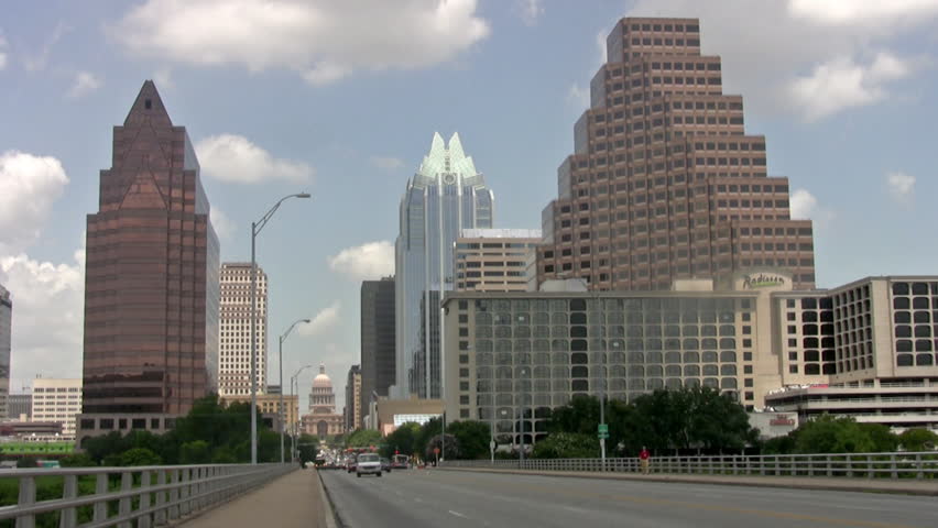Video wide view of downtown Austin Texas. State Capitol building at end of street. View from Bridge with businesses, office and hotels. Traffic passing.