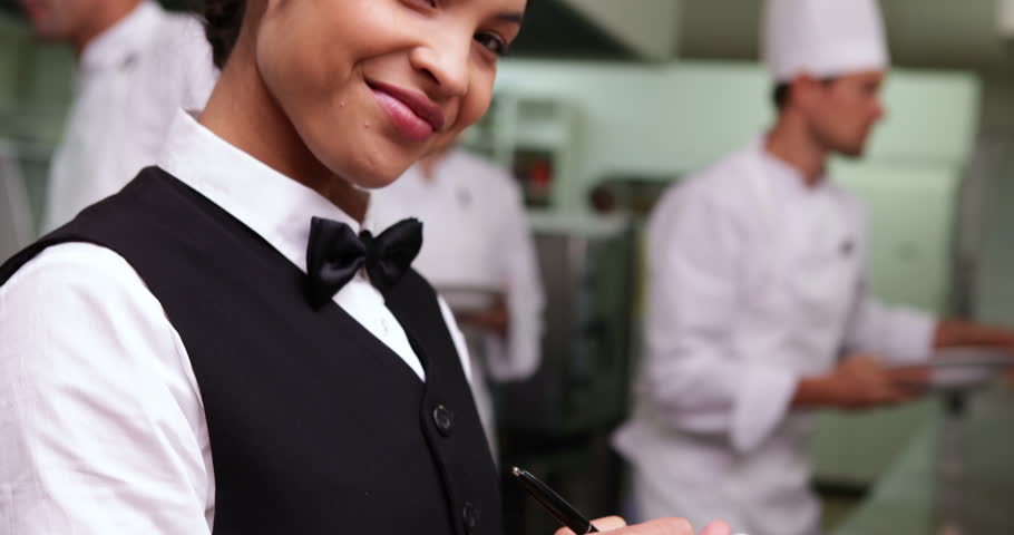 Smiling waitress writing on her notepad in a commercial kitchen