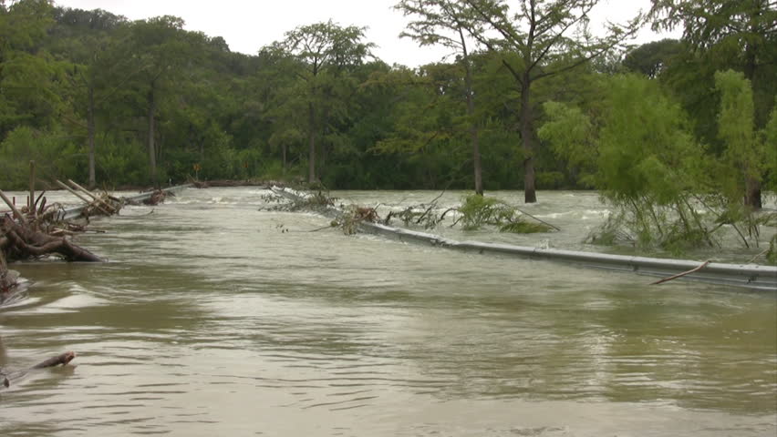Video closeup of a flooded road in south Texas after massive tropical rain storms. Forest country area. Road and guard rail disappearing into swollen river. 