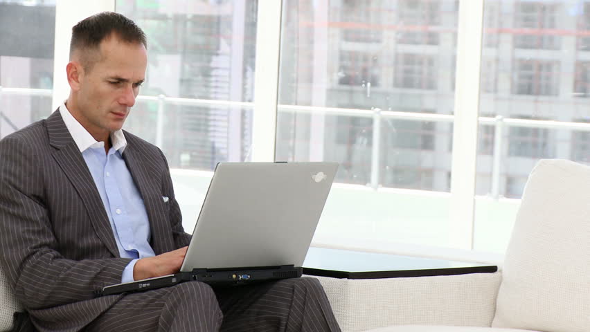 Handsome business man working at a laptop sitting on sofa