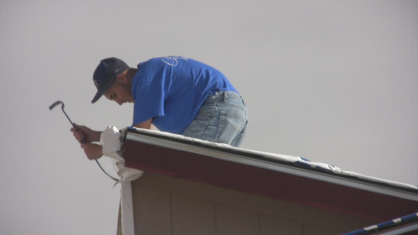 Young Hispanic man working on roof of a new mobile home to remove shipping materials.