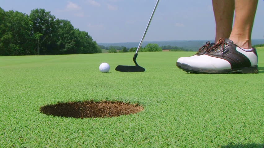 Close-up of golfer using putter to sink short putt into hole, with shotgun audio.

