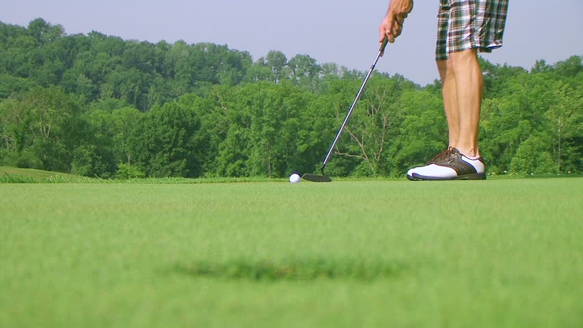 Close-up of golfer using putter to sink long putt into hole, rack focus with shotgun audio.

