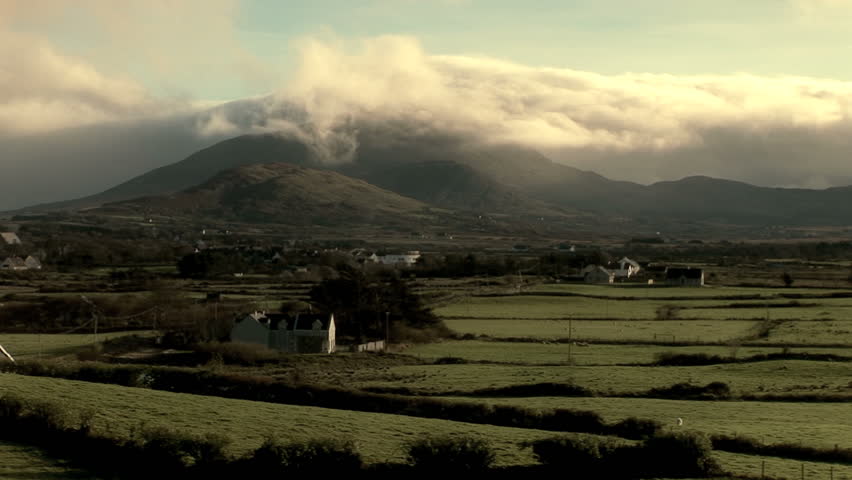 Clouds hug the tip of Croagh Patrick Mountain in Ireland.  The Irish hillside is in the foreground. 