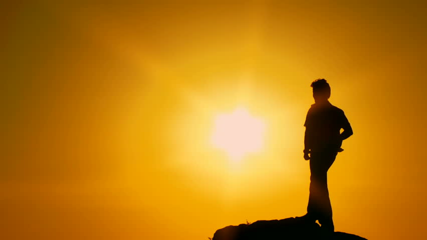 Bright sun. Silhouette. Motion zoom. A man stands on the edge of a cliff and looks at the sun through his hand.