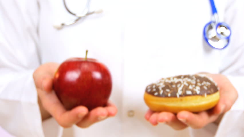 Doctor in white coat offering a fresh apple as an alternative to a sugary doughnut as a healthy food option