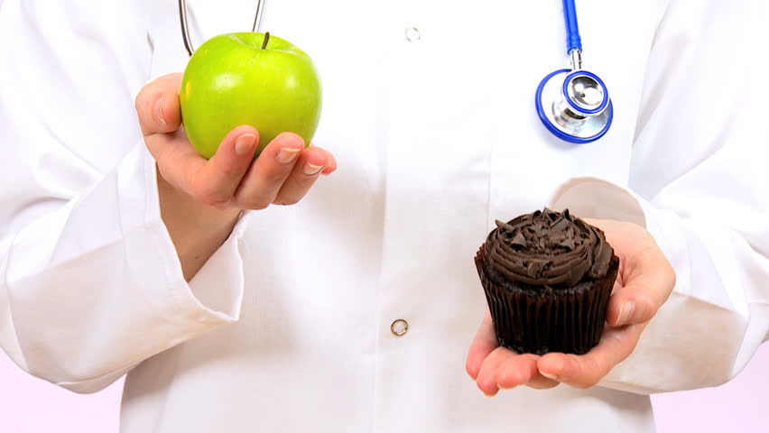 Doctor in white coat weighing up the choice between fresh fruit or sugary muffin as a healthy food option