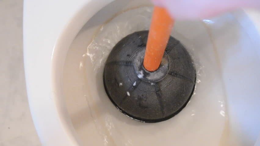 Hands take a toilet plunger and unclog a toilet.