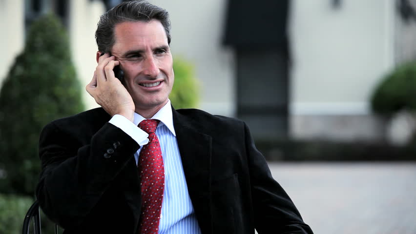 Confident business executive at outdoor cafe receiving good news on his cell phone