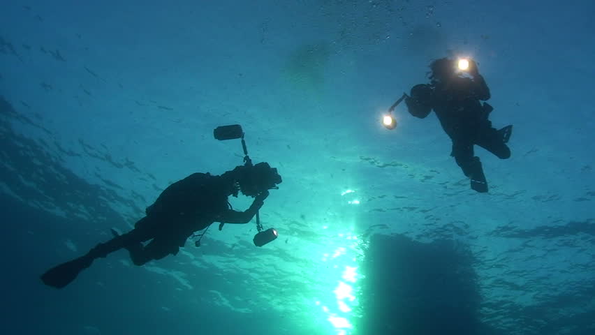 Low angle silhouette view of two scuba divers with underwater cameras.
