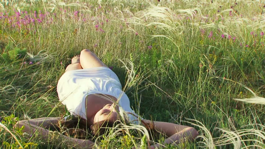 Girl resting on the nature. Beautiful girl lying on the field. Then the rolls from the back to back. Moving camera.