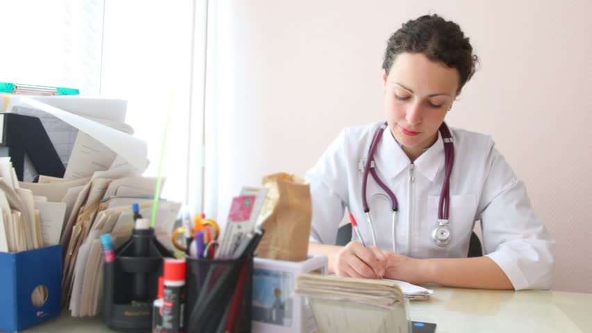 Female doctor with stethoscope around her neck makes an entry in a patient record in her office