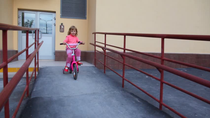 little girl with rucksack pedaling on bicycle near apartment block