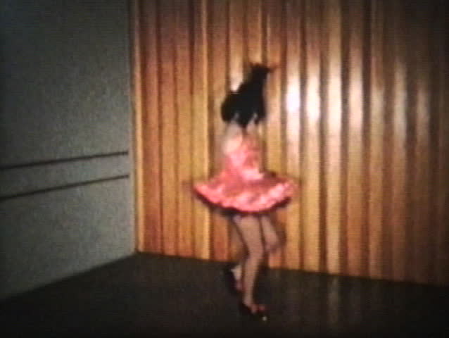 A teenage girl wearing a pink dress goes through her tap dancing routine. 