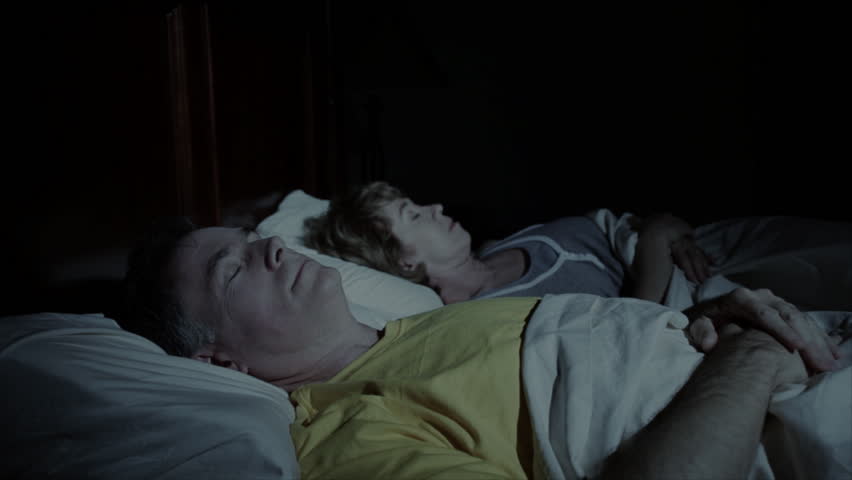 A woman awakened by her husbands loud snoring covers her ears in an effort to deal with the noise.