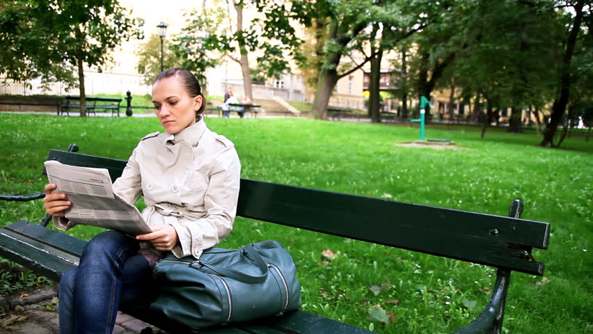 Woman sitting in the park and reading newspaper, dolly shot 