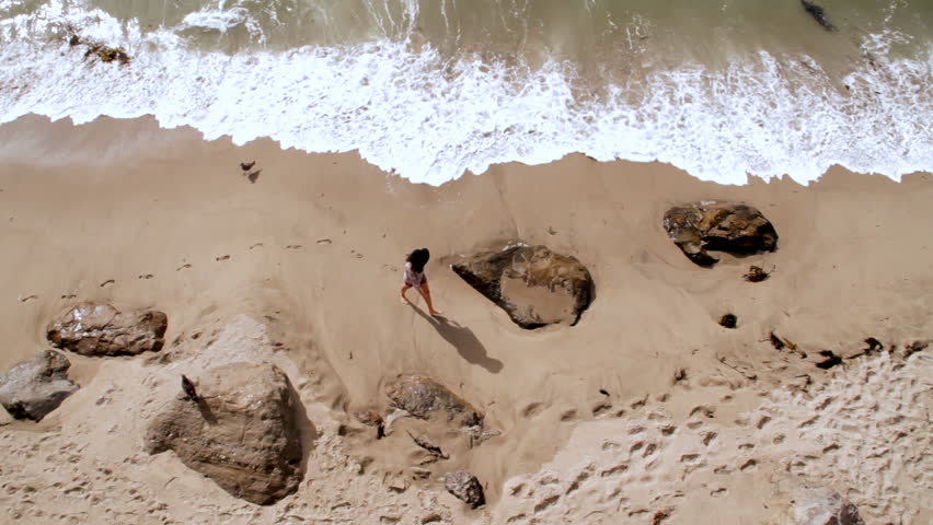 A woman walks alone on a rocky California beach.