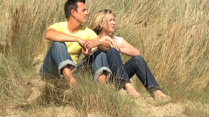 Attractive young caucasian couple enjoying quiet time together sitting in sand dunes at the coast  filmed at 60FPS