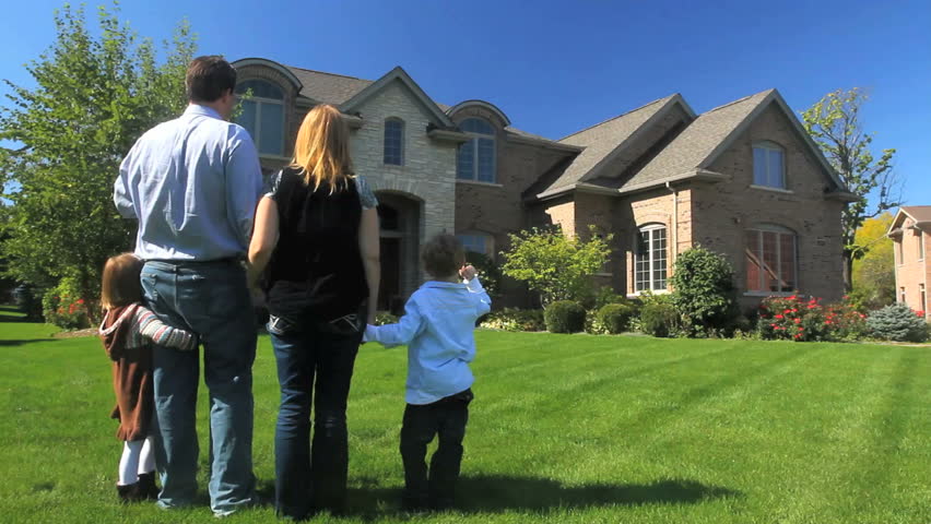 A family stands together in their yard, facing their luxury home 